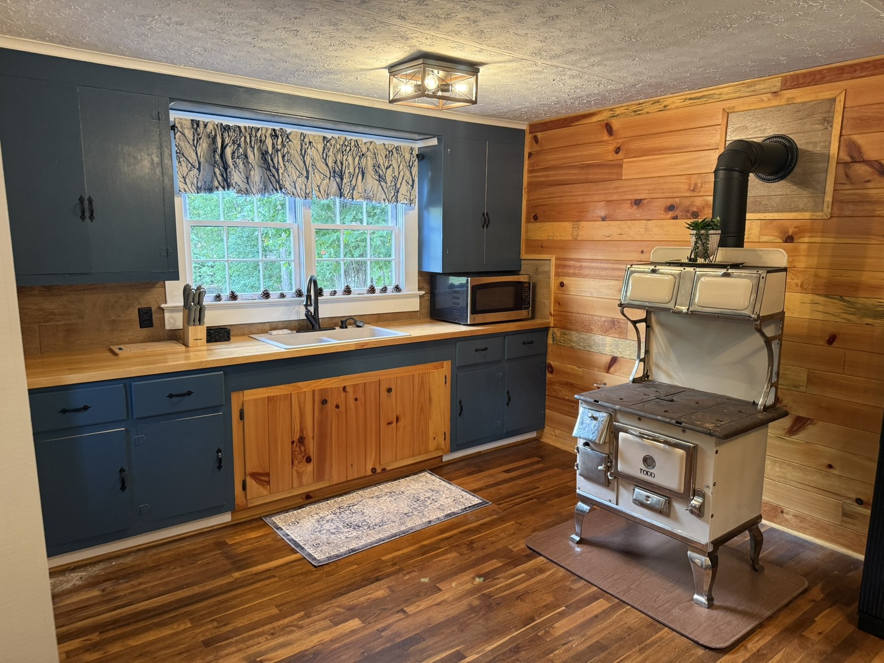 Cottage kitchenette with blue cabinets, a sink beneath the window, and wood walls