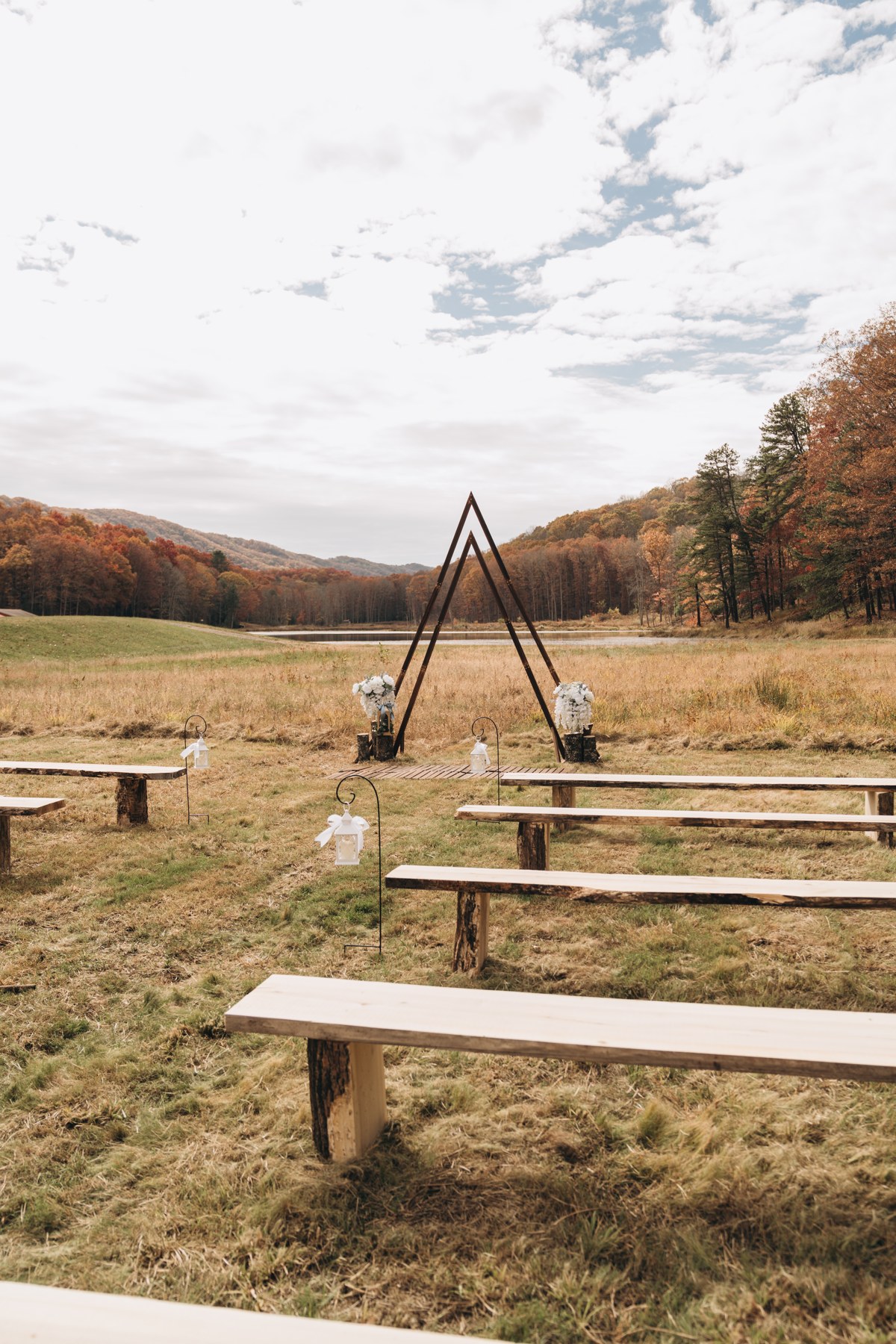 Wooden benches and a triangular wedding arch facing the lake and autumn hills