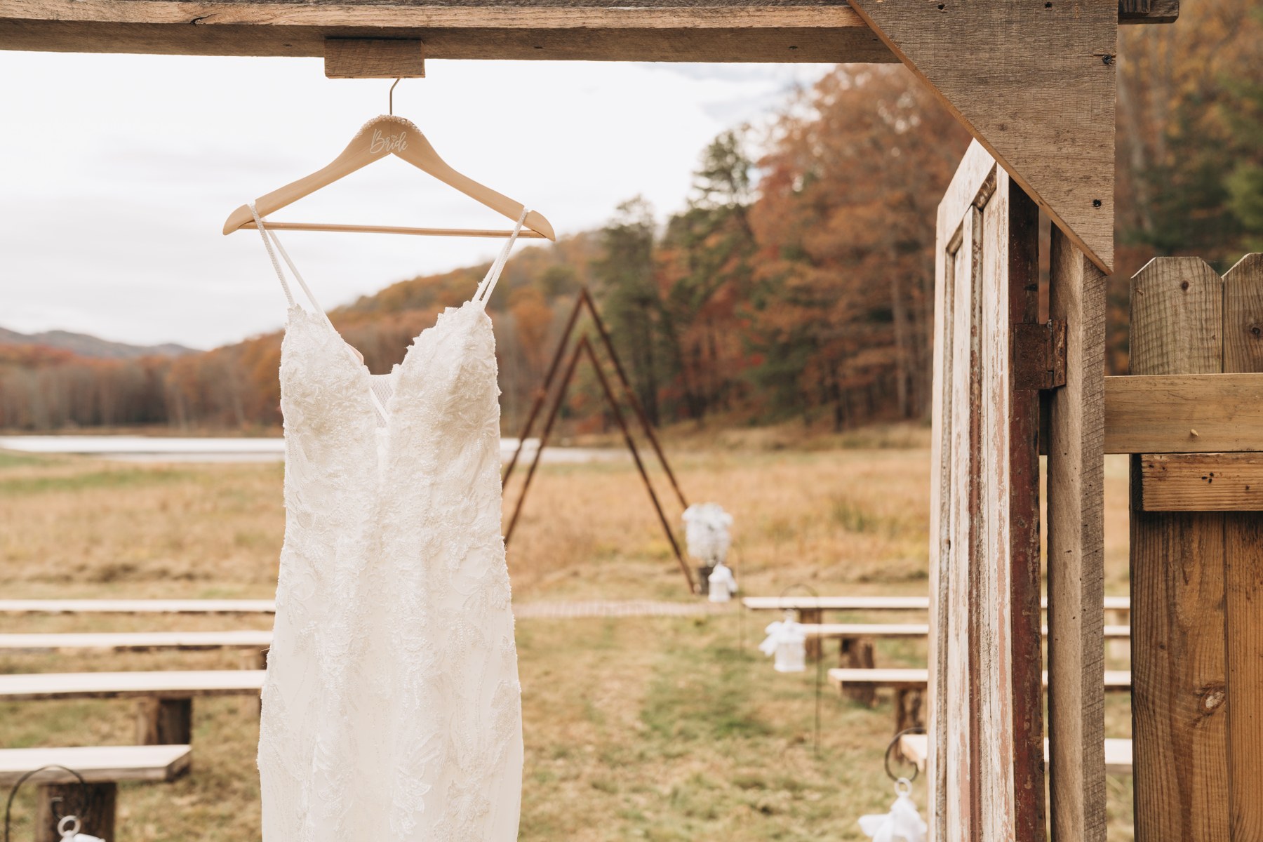 A wedding dress hanging from a wooden beam overlooking the lakeside ceremony setting